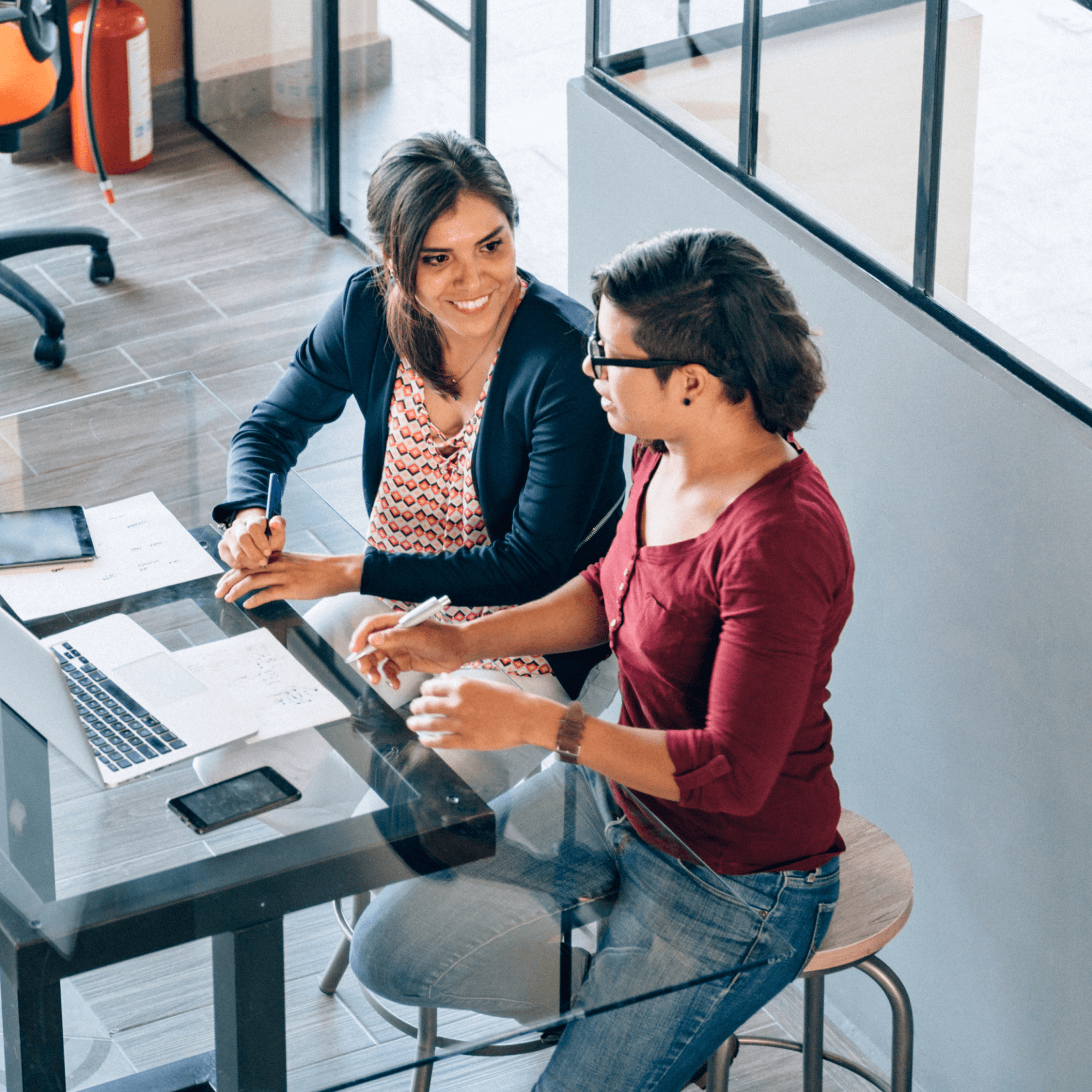 Two people sitting at a desk talking to one another