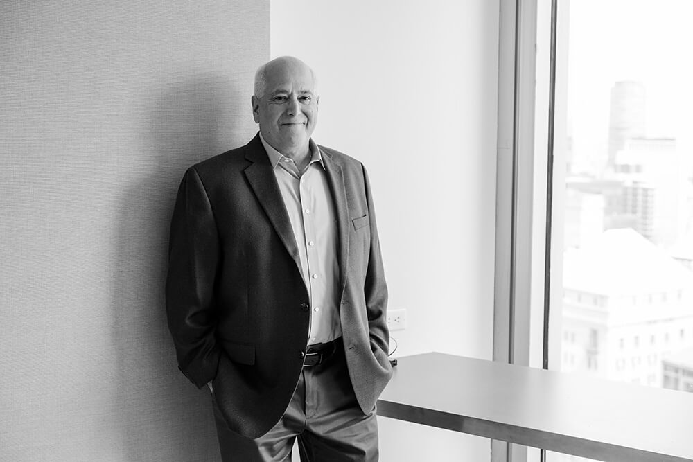 Black and white photo of a person in a suit standing and smiling at the camera