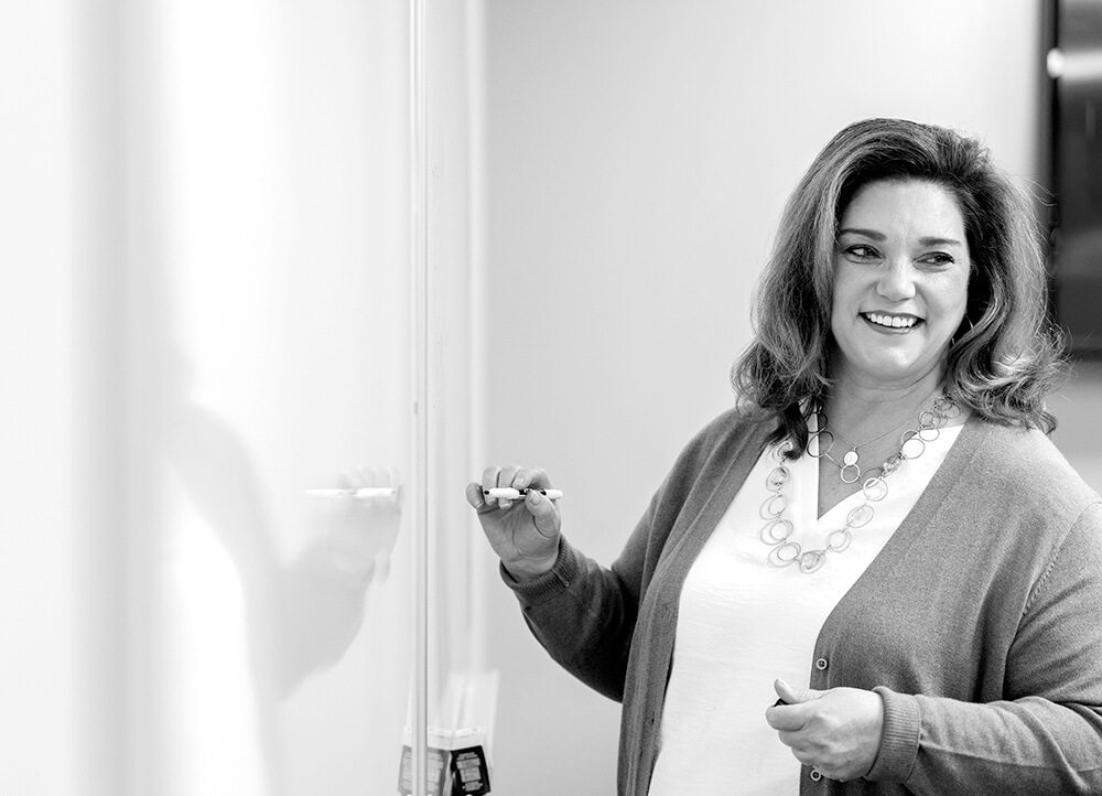 Black and white photo of a person smiling at a whiteboard