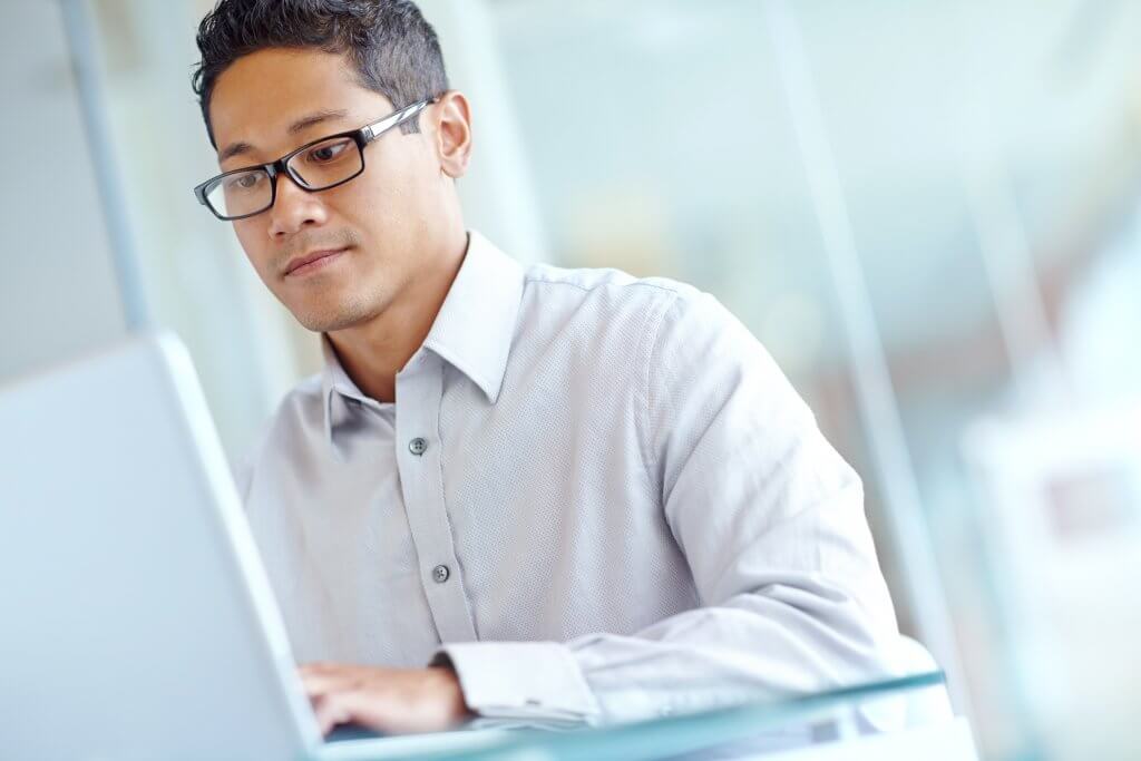 Person in white shirt with glasses typing on computer.