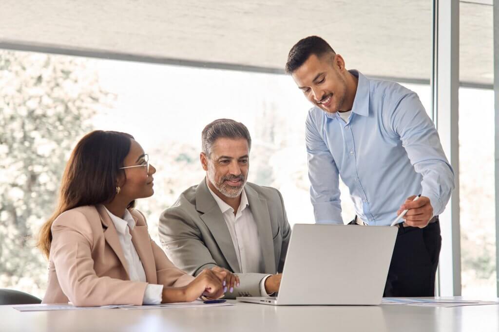 Three business professionals collaborating at a table with a laptop in an office.