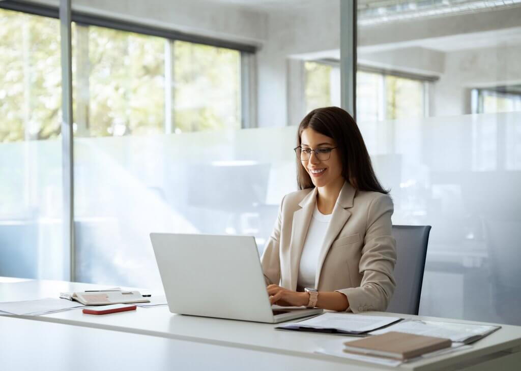 Person in an office setting, using a laptop, dressed in a beige blazer.